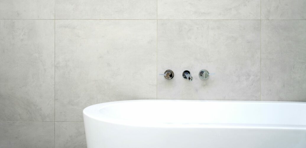 シンプルなグレーのタイル壁と白いバスタブだけが写る、一日の終わりの静かなバスルーム