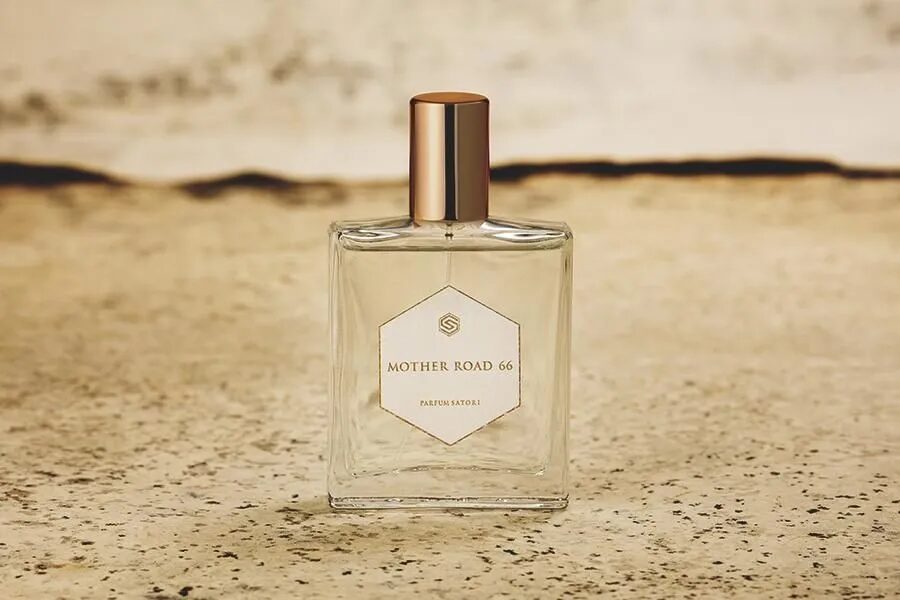 A high-resolution promotional close-up of the current MOTHER ROAD 66 perfume bottle, highlighting its sleek design and clear fragrance liquid.